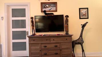 Una habitación con un televisor montado en un mueble de madera, una puerta con paneles de vidrio esmerilado y una estatua de jirafa.