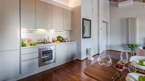 A modern kitchen with stainless steel appliances, wooden flooring, and a dining area with a table set for two. - De Nobili Penthouse in Lucca (Lucca)