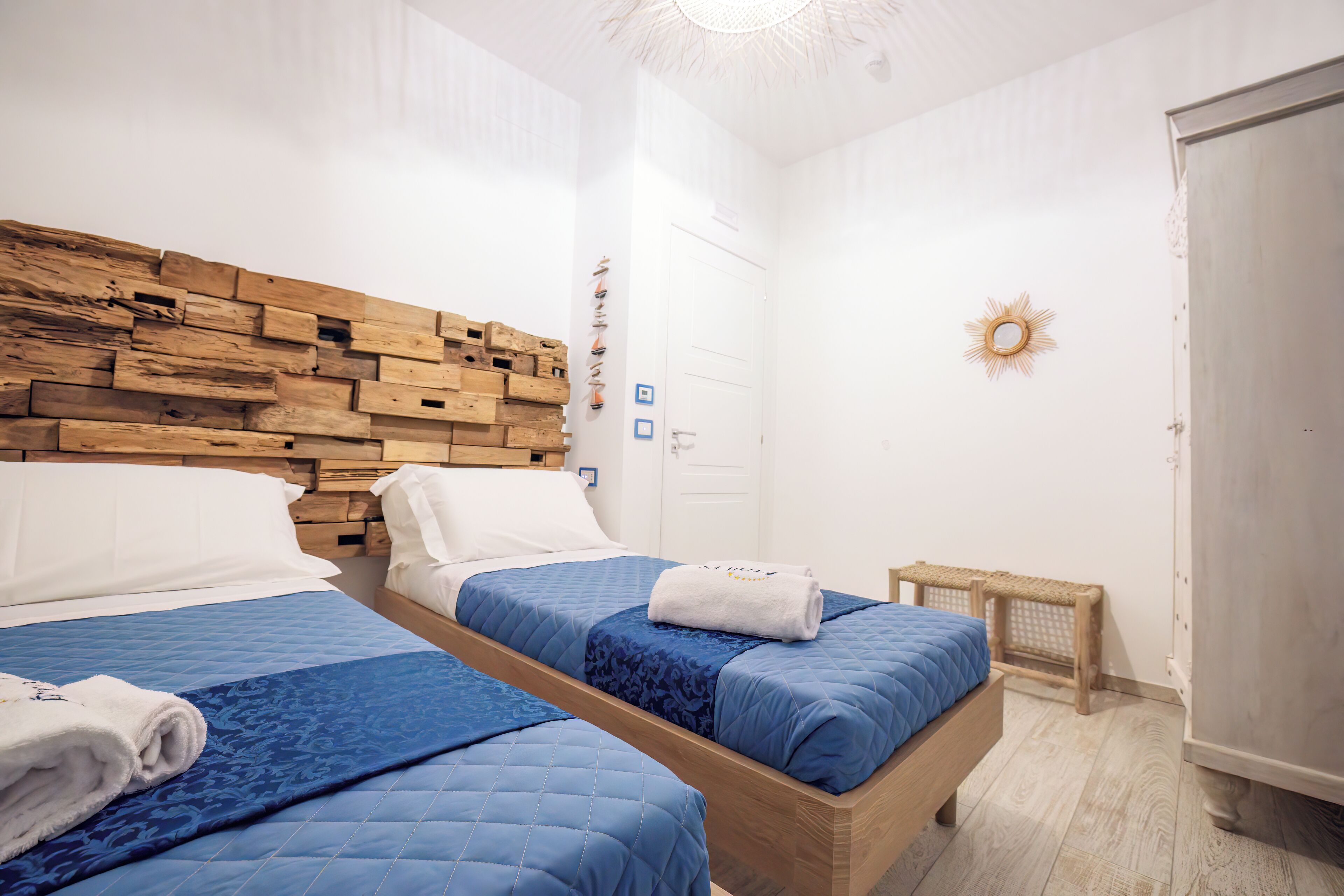 A hotel room with two beds, wooden headboard, white walls, and a small window.