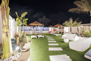 A nighttime outdoor area with artificial grass, white lounge chairs, and thatched umbrellas. - Étoiles Luxury Guest House Resort  (Palmi)