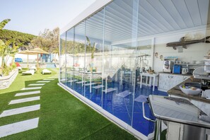 A modern outdoor pool area with glass walls, a dining area, and a kitchen visible through the glass. - Étoiles Luxury Guest House Resort  (Palmi)