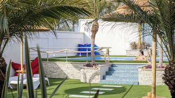 Un espace piscine agrémenté d’un mur en pierre, d’une petite piscine et d’un coin salon avec une chaise blanche et des coussins rouges.