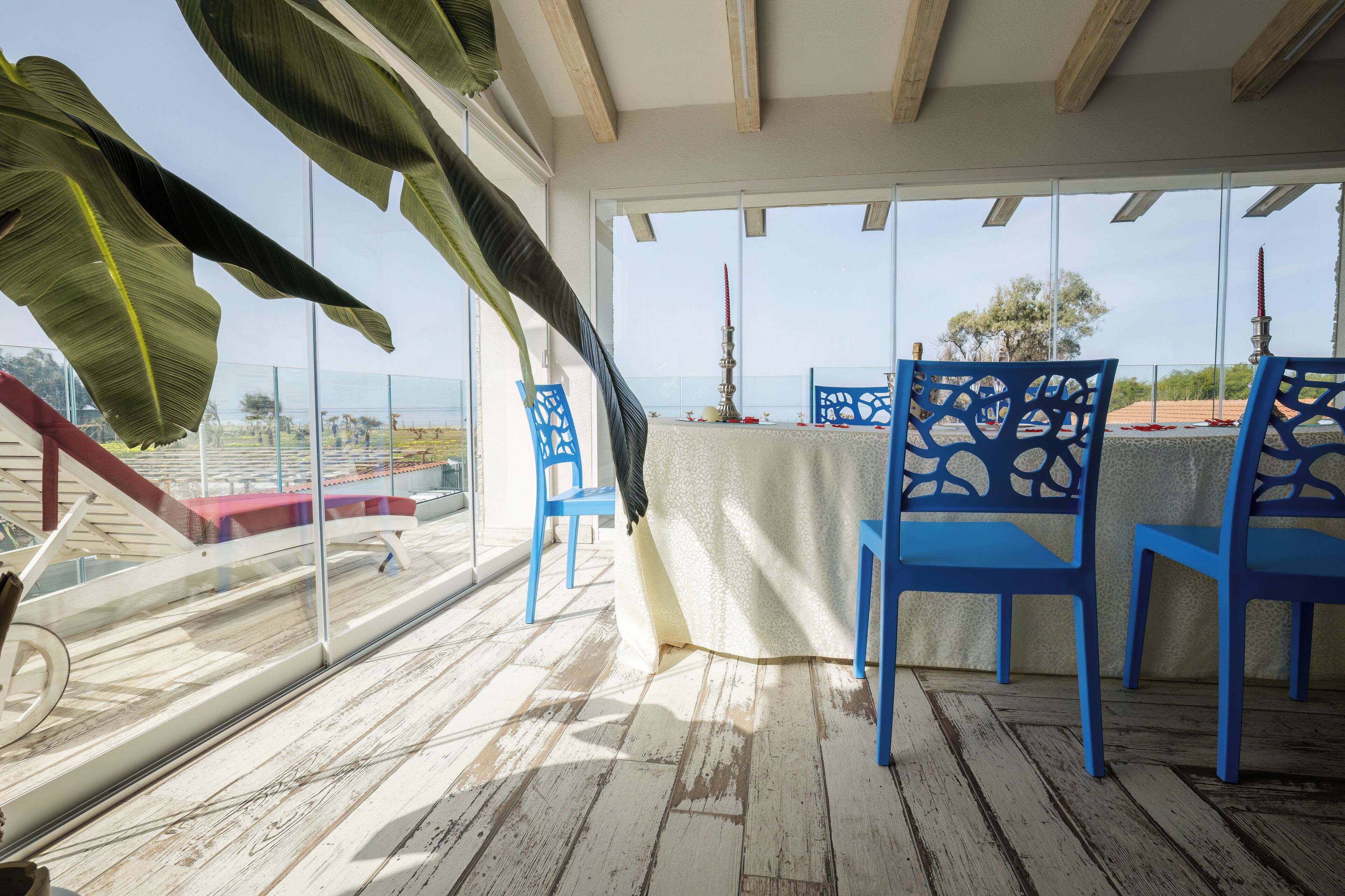 A balcony with blue chairs, a table, and a view of the beach.
