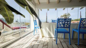 A balcony with blue chairs, a table, and a view of the beach.