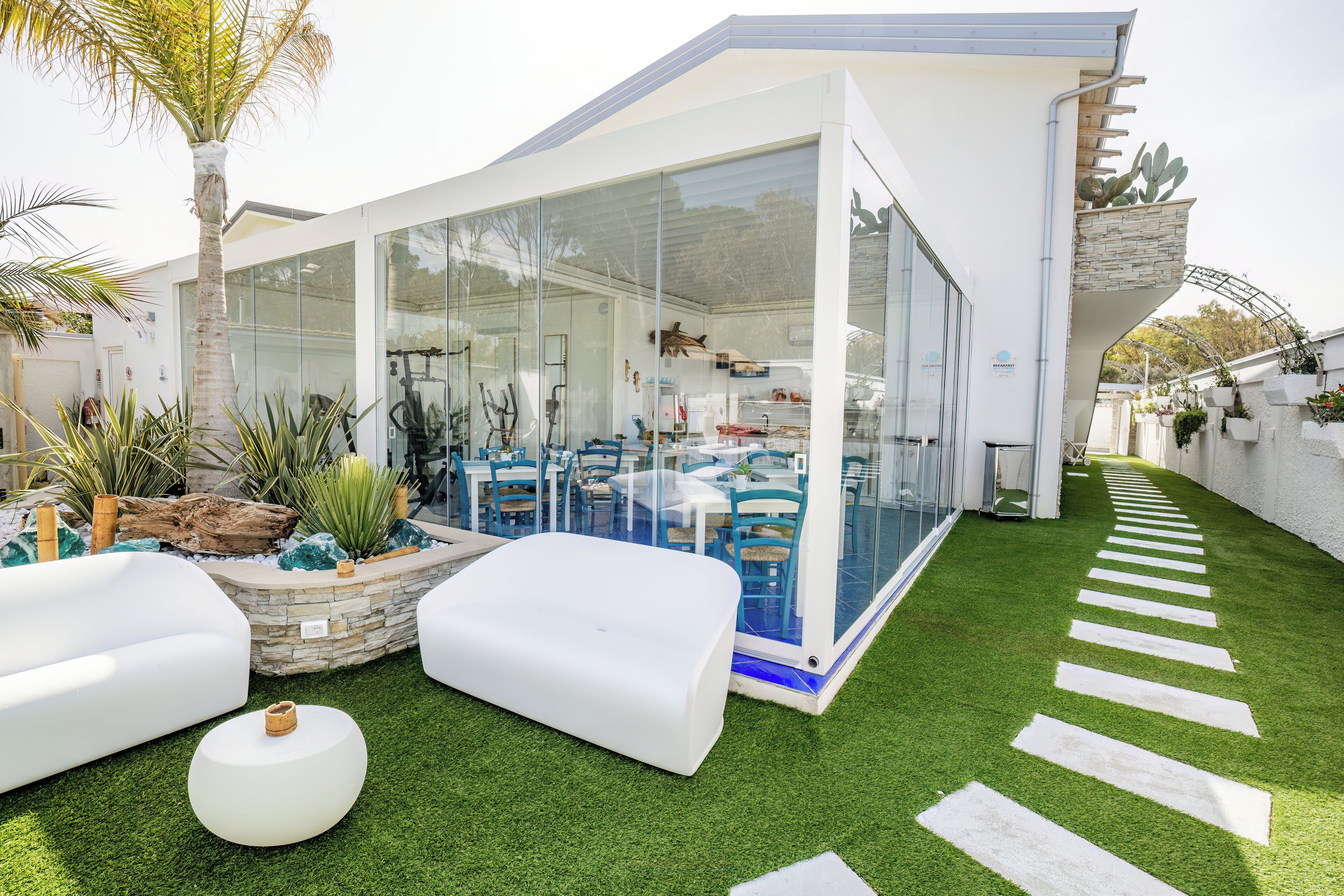 Eine moderne Außenpatio mit Kunstgrasanlage, weißer Möbel und einem wintergartenartigen Essbereich.