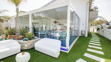 Eine moderne Außenpatio mit Kunstgrasanlage, weißer Möbel und einem wintergartenartigen Essbereich.