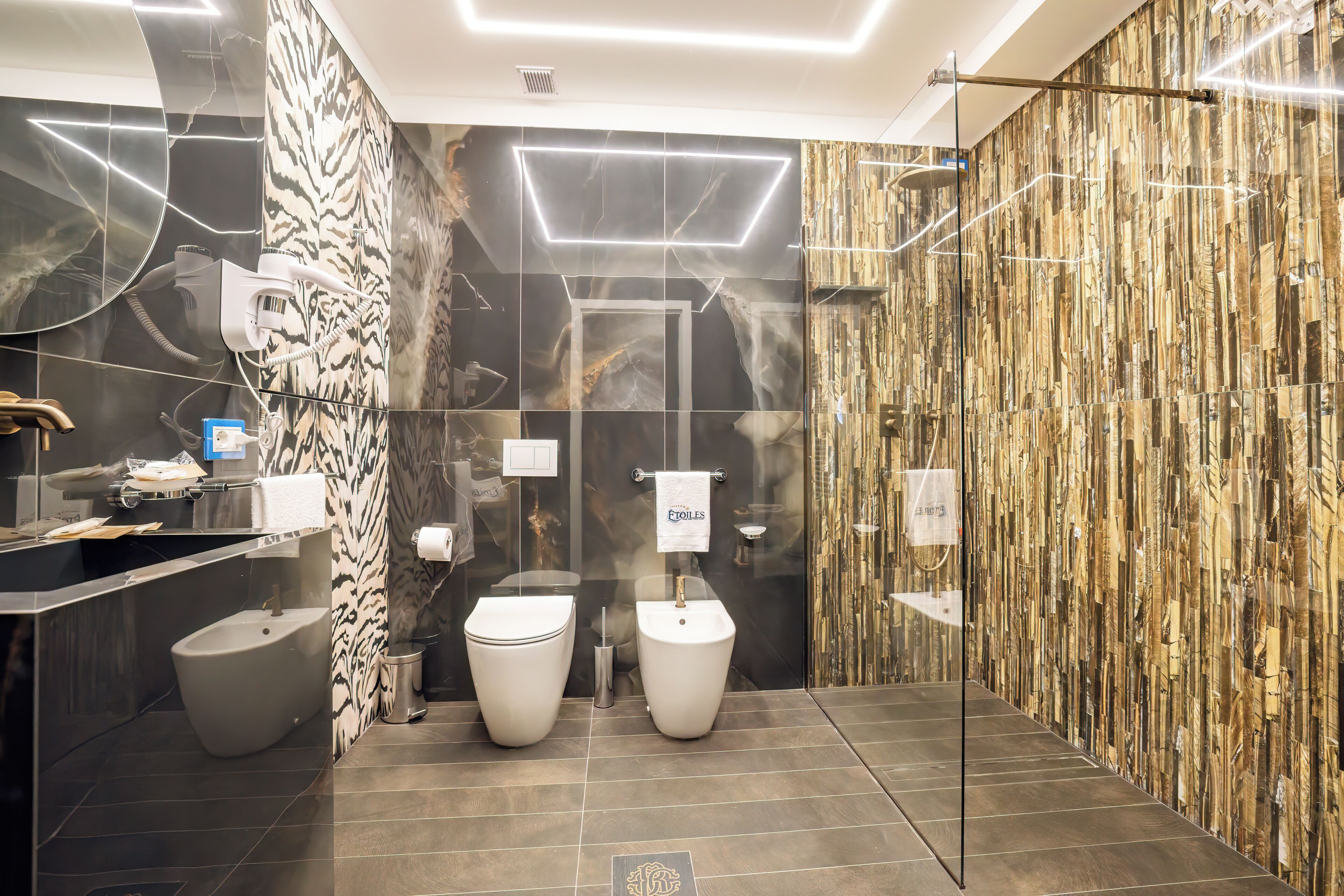 A modern bathroom with two toilets, a bidet, a vanity with a mirror, and a towel rack.