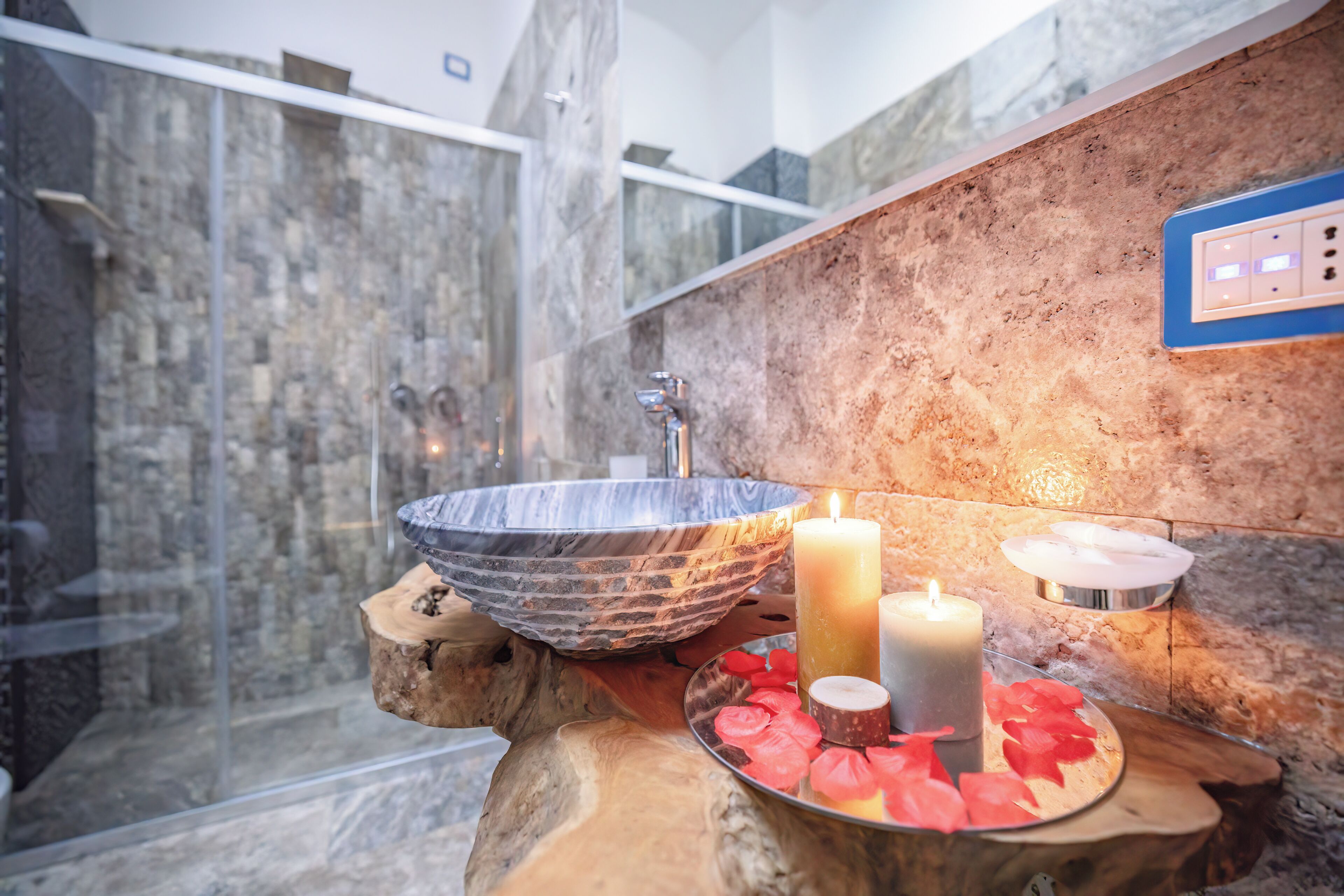 A bathroom with a stone sink, candles, and a wooden tray with rose petals.