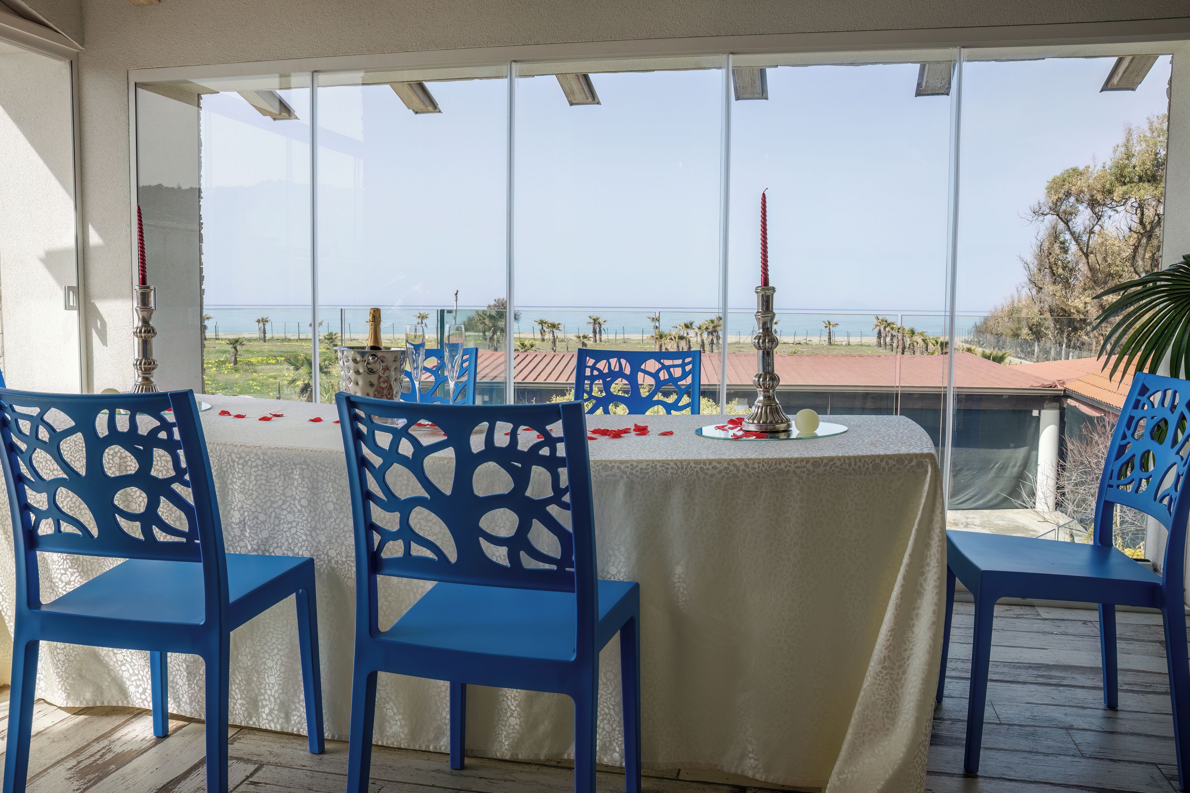 A dining area with a table set for four, blue chairs, and a view of the sea.