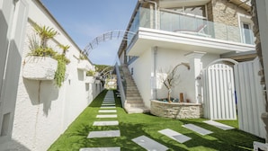 Una casa moderna de dos pisos con una escalera que conduce al nivel superior, fachada blanca y un pequeño jardín con piedras a modo de camino.