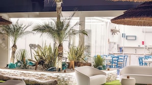 Un espacio interior moderno con pared de piedra, palmeras y mobiliario blanco.