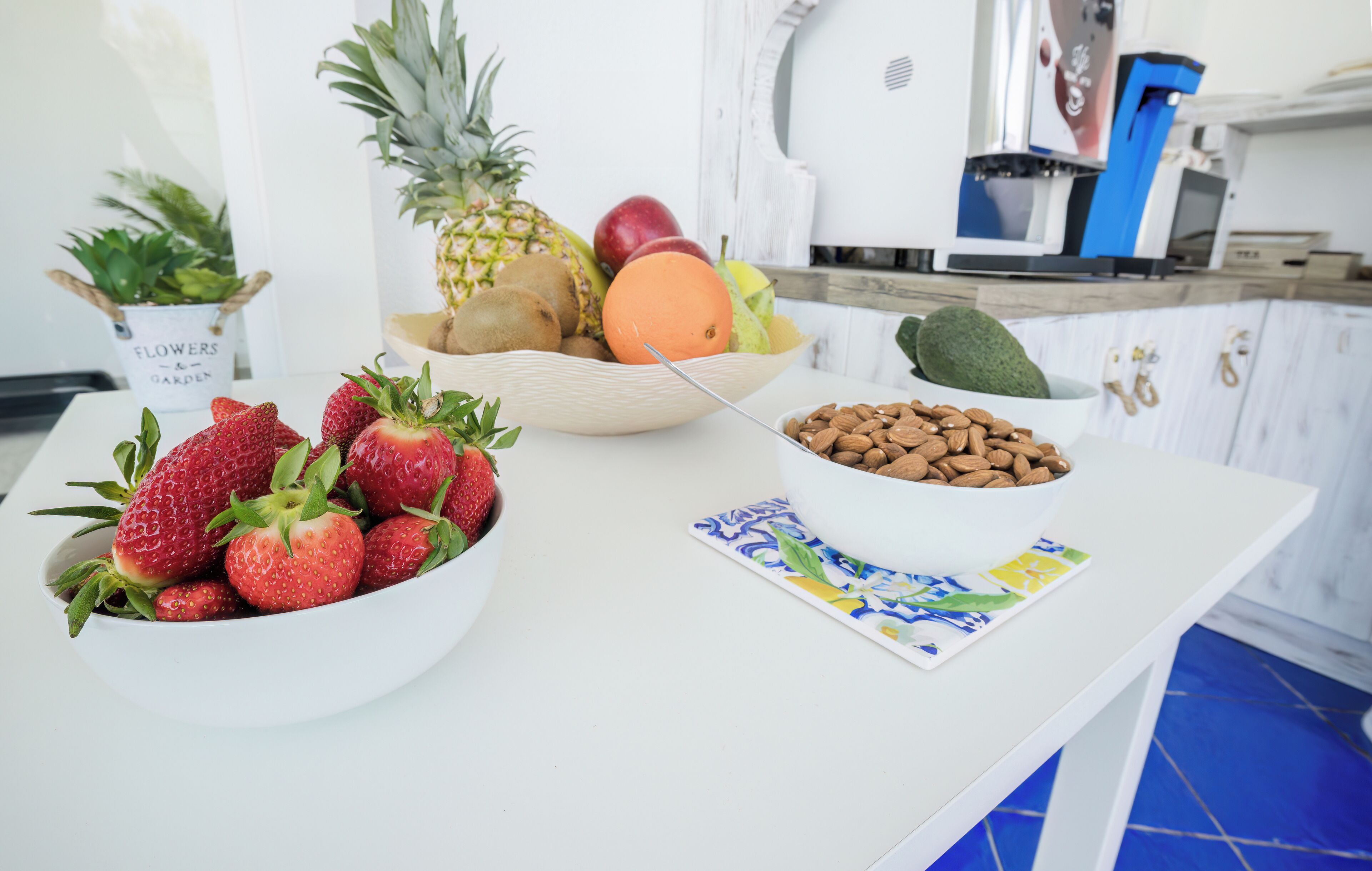 A kitchen counter with a bowl of strawberries, a bowl of mixed fruits, a bowl of almonds, and a coffee machine.