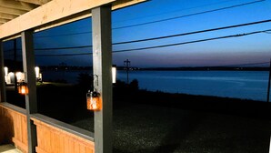 Un área de estar al aire libre con techado, con bancos de madera y luces tipo farol, con vista a un cuerpo de agua.