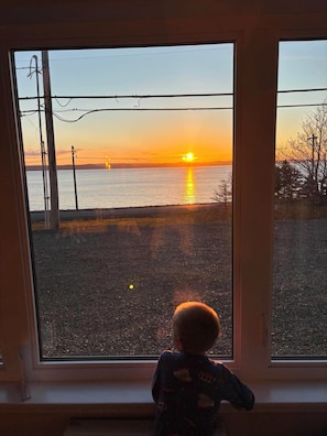 A child looking out of a window at a sunset over water.