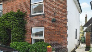 A two-story brick house with a white exterior, a visible chimney, and a small garden area with a potted plant. - 2 bedroom accommodation in Lydd, Romney Marsh (Lydd, Romney Marsh)