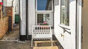 A narrow alleyway with a white metal bench, a potted plant, and a window with blinds. - 2 bedroom accommodation in Lydd, Romney Marsh (Lydd, Romney Marsh)