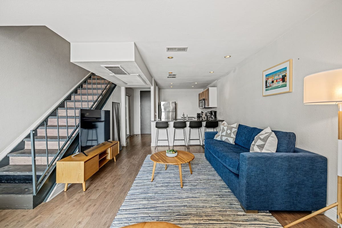A modern living room with a blue sofa, wooden coffee table, and a staircase leading to an upper floor.