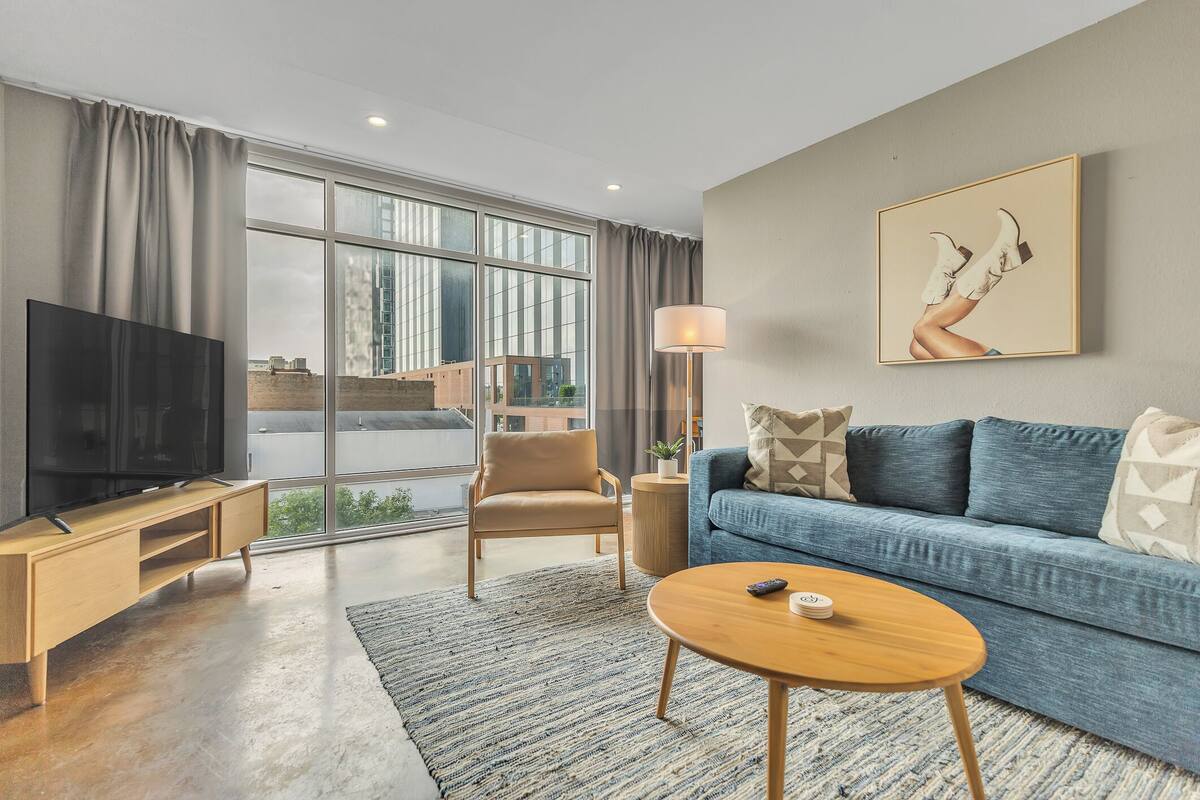 A modern living room with a TV, sofa, coffee table, and large windows.