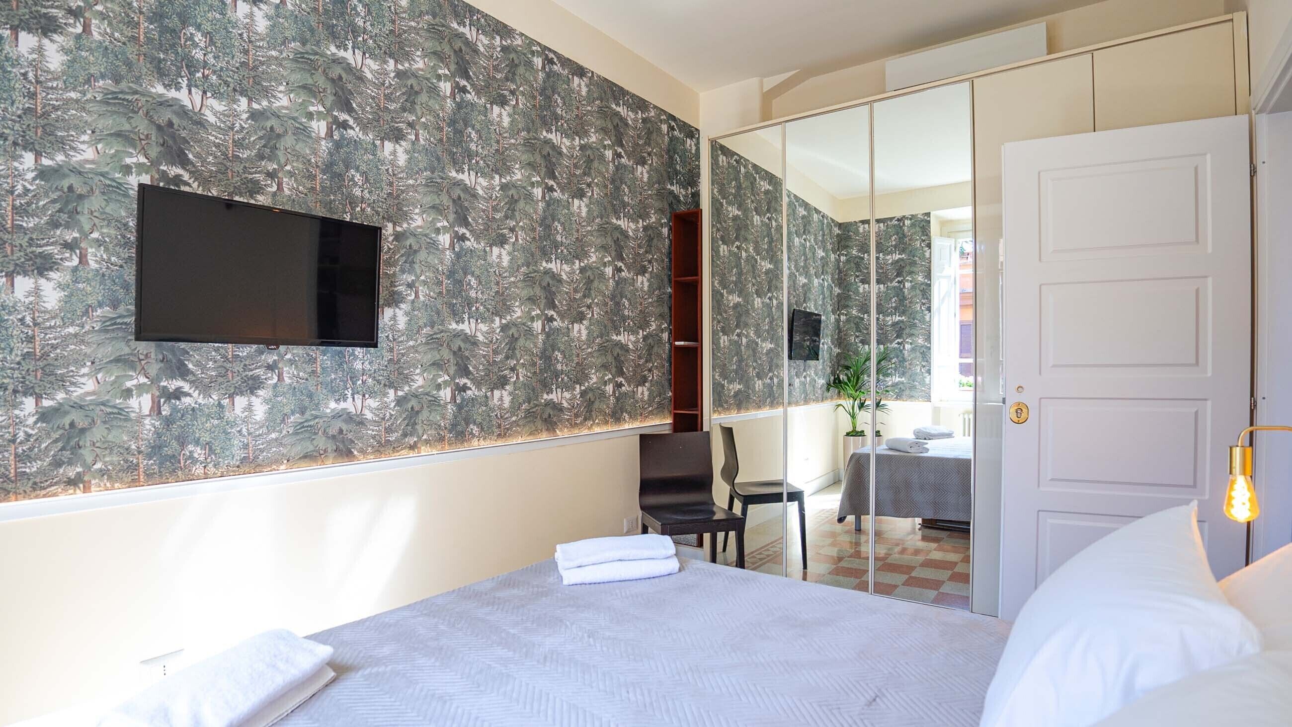 A hotel room with a bed, a TV mounted on the wall, a mirror, and a door leading to a balcony.