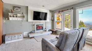 A living room with a fireplace, a mounted TV, and a view of the outdoors. - Picturesque Mt Spokane Condo Near Skiing & Biking! (Mead)