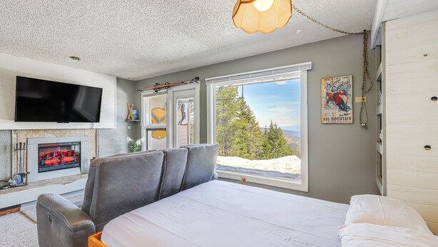 A bedroom with a bed, a TV mounted on the wall, a fireplace, and a large window with a view of trees and mountains. - Picturesque Mt Spokane Condo Near Skiing & Biking! (Mead)