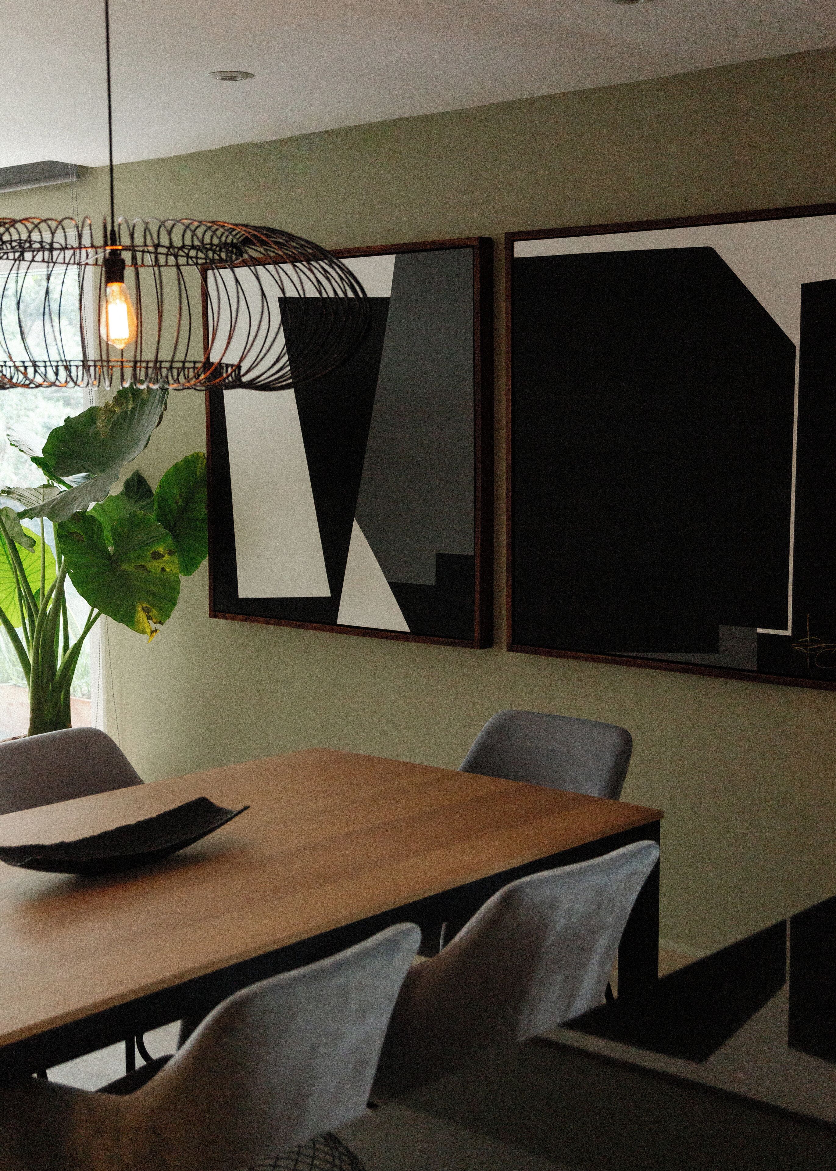 A modern dining area with a wooden table, grey chairs, a hanging light fixture, and abstract wall art.