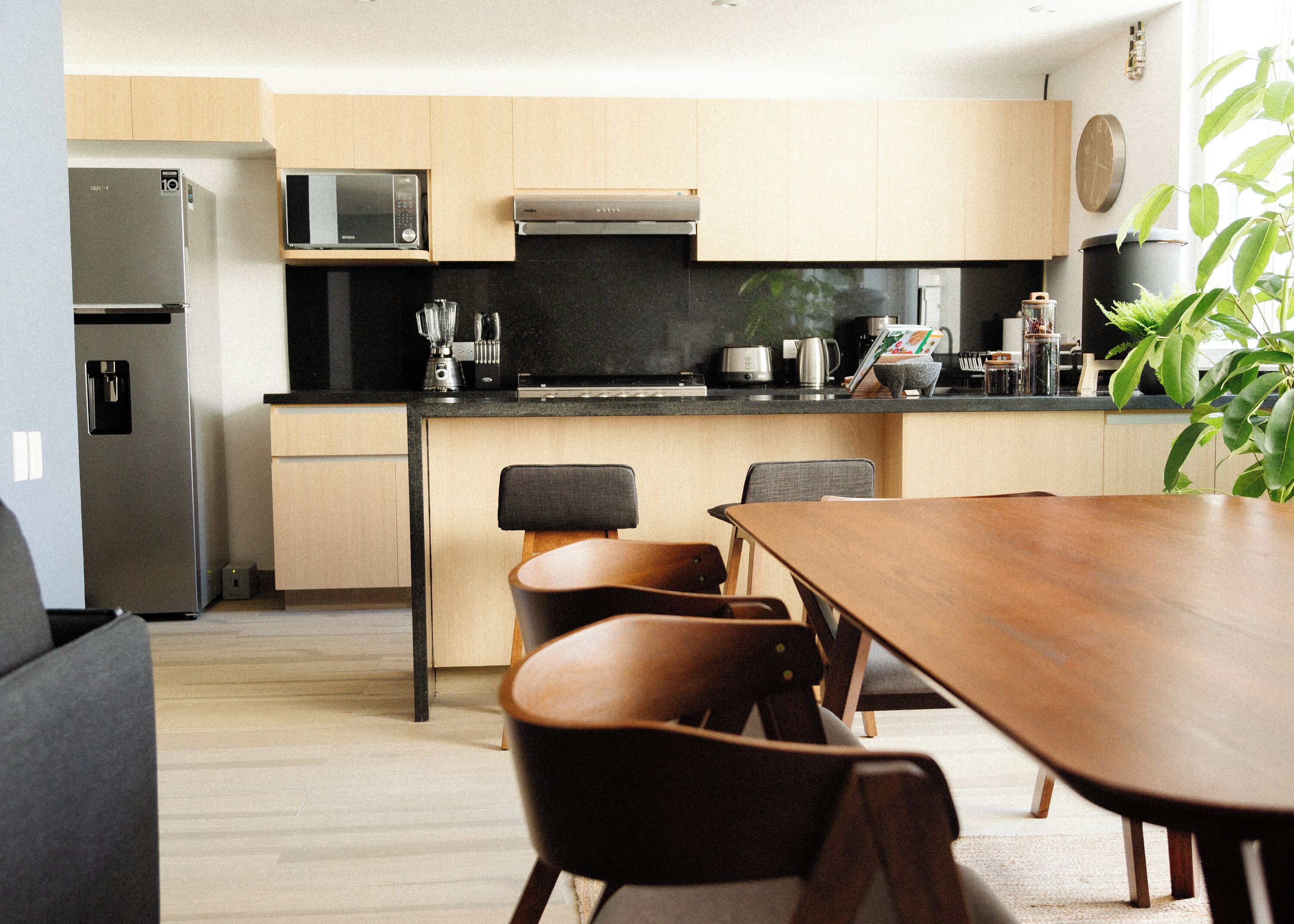 A modern kitchen with a dining area, including a wooden table and chairs, a refrigerator, microwave, and various kitchen appliances.