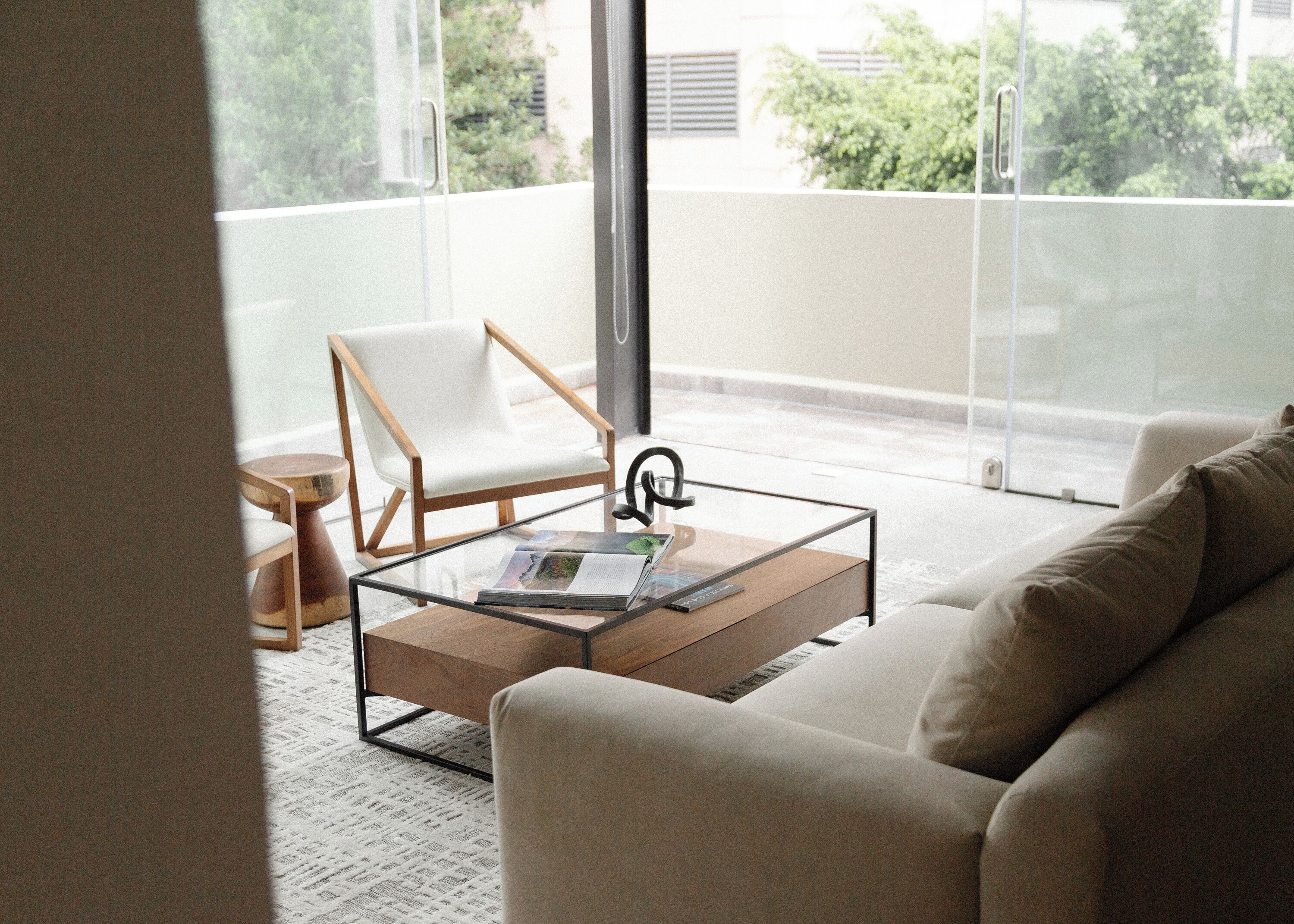 A modern living room with a glass coffee table, a beige sofa, and a white chair.
