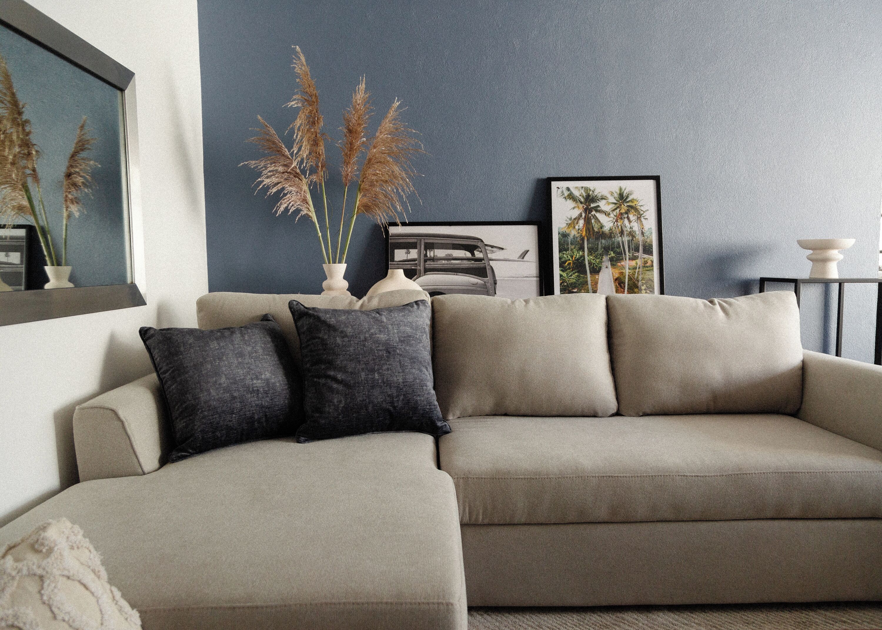 Un salon avec un canapé d’angle beige, un mur d’accent bleu foncé et des plantes décoratives.