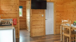 L’intérieur d’une cabane en bois comprend un coin cuisine, une table à manger avec des chaises et un téléviseur fixé au mur.