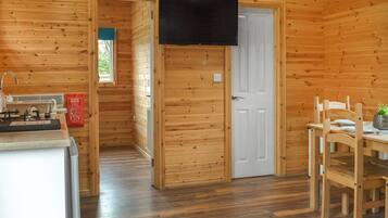 A wooden cabin interior with a kitchen area, a dining table with chairs, and a television mounted on the wall.
