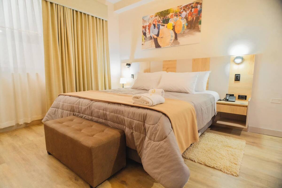 Une chambre d’hôtel avec un grand lit, une table de chevet avec une lampe, une tête de lit en bois et un tableau au mur.