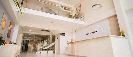 A hotel lobby with a reception desk, a staircase, and a glass railing on the upper level.