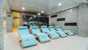 A spa room with multiple sun loungers, a large window, and a wall-mounted screen displaying a relaxing scene. - Sauna & Suite Puñuykuna (Cajamarca)