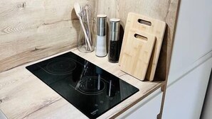 Une cuisine dotée d’un plan de travail en bois, d’une plaque de cuisson à induction noire, d’une bouilloire en acier inoxydable, d’une planche à découper en bois et d’un bloc à couteaux.