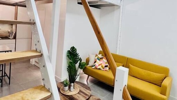 Un intérieur moderne avec un escalier, un canapé jaune et une table ronde en bois.
