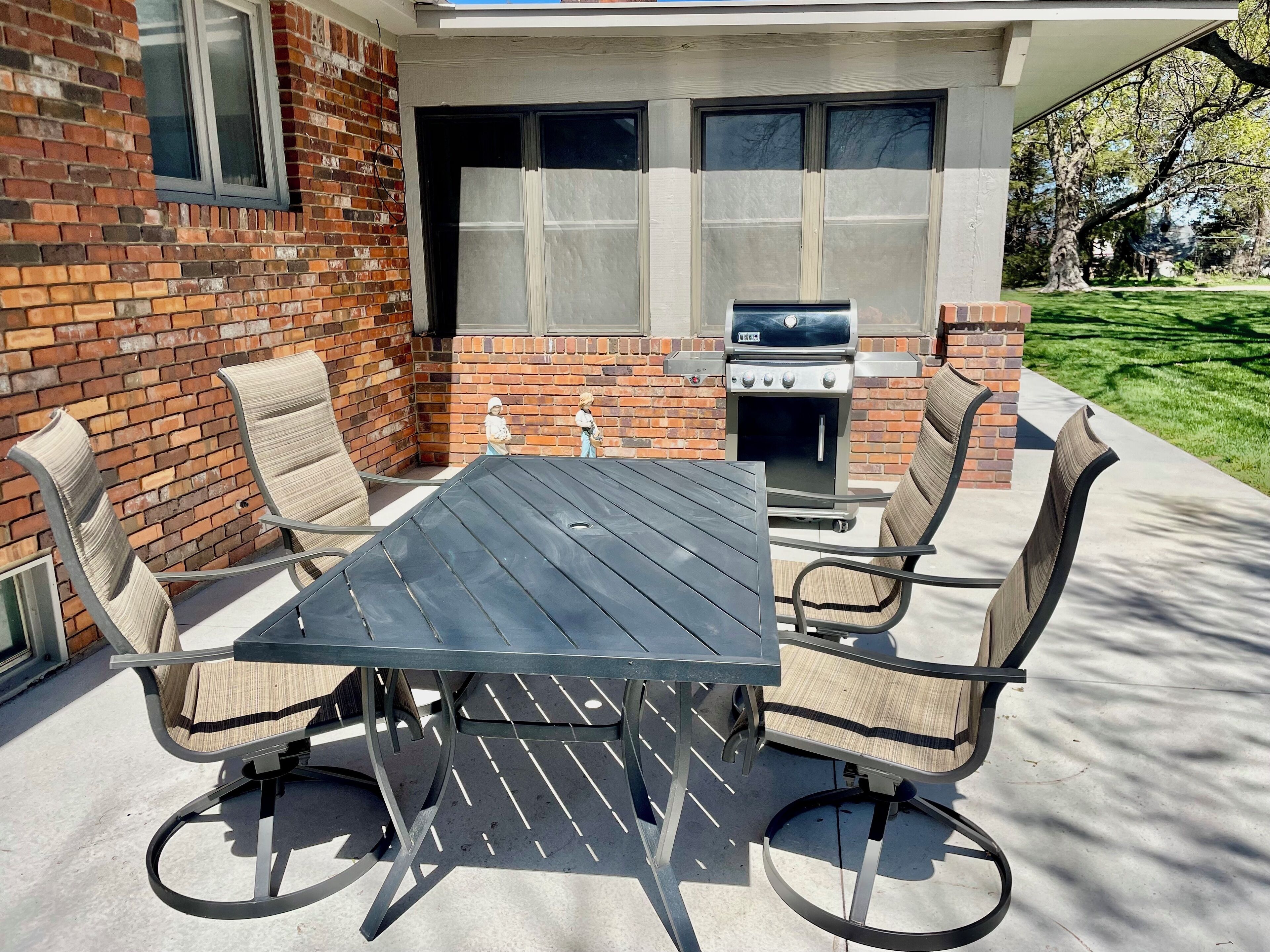 Un patio exterior con pared de ladrillo, una parrilla y una mesa con sillas.