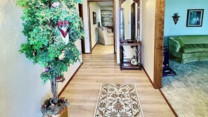A hallway with a chandelier, a potted tree, a patterned rug, and a green couch in the background.