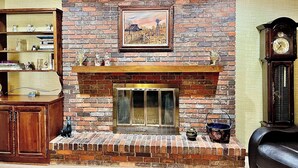 A brick fireplace with a mantel, a framed painting above it, and a wooden cabinet to the left.