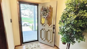A hallway with a patterned carpet, a door with a decorative glass panel, and a potted plant.