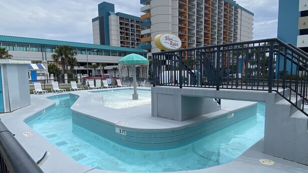 Ein Schwimmbecken mit einer Wassersäule, einem Schild mit der Aufschrift 'Wave Rider' und einer '3 FT' Tiefenmarkierung.