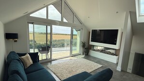 Una sala moderna con un sofá grande, un televisor de pantalla plana y un ventanal corredero que da a un balcón.