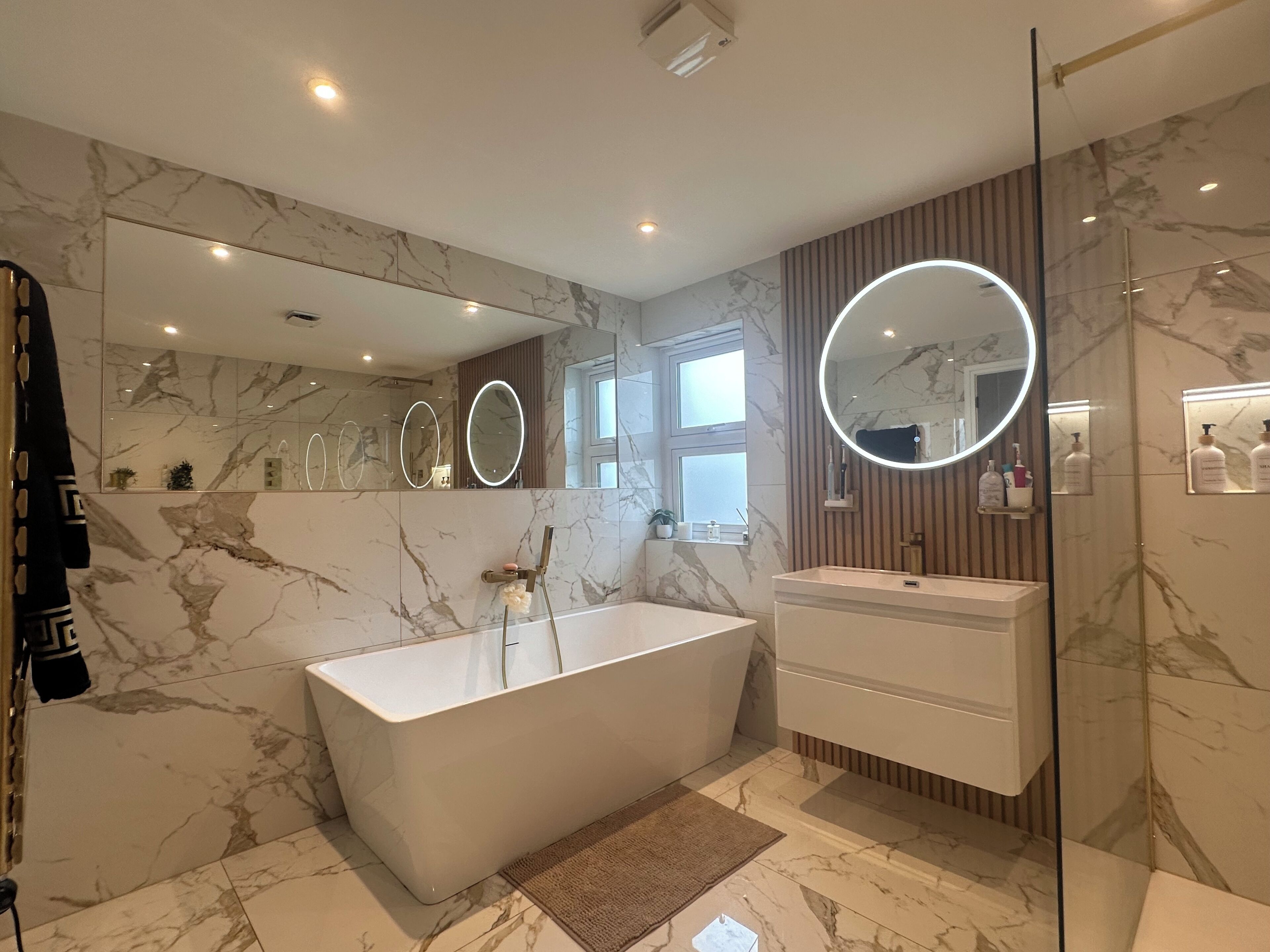 A modern bathroom with a freestanding bathtub, a vanity with a mirror, and marble flooring.