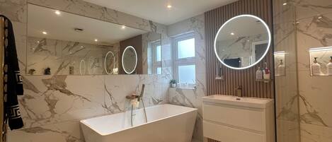 A modern bathroom with a freestanding bathtub, a vanity with a mirror, and marble flooring.