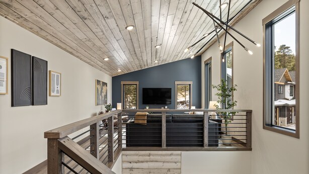 Een ruime loft met een hoge plafond, houten balken, een entresol met een zwarte bank, een televisie en grote ramen met uitzicht op buiten.