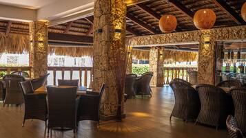 A restaurant with wicker furniture, stone pillars, and hanging lanterns.