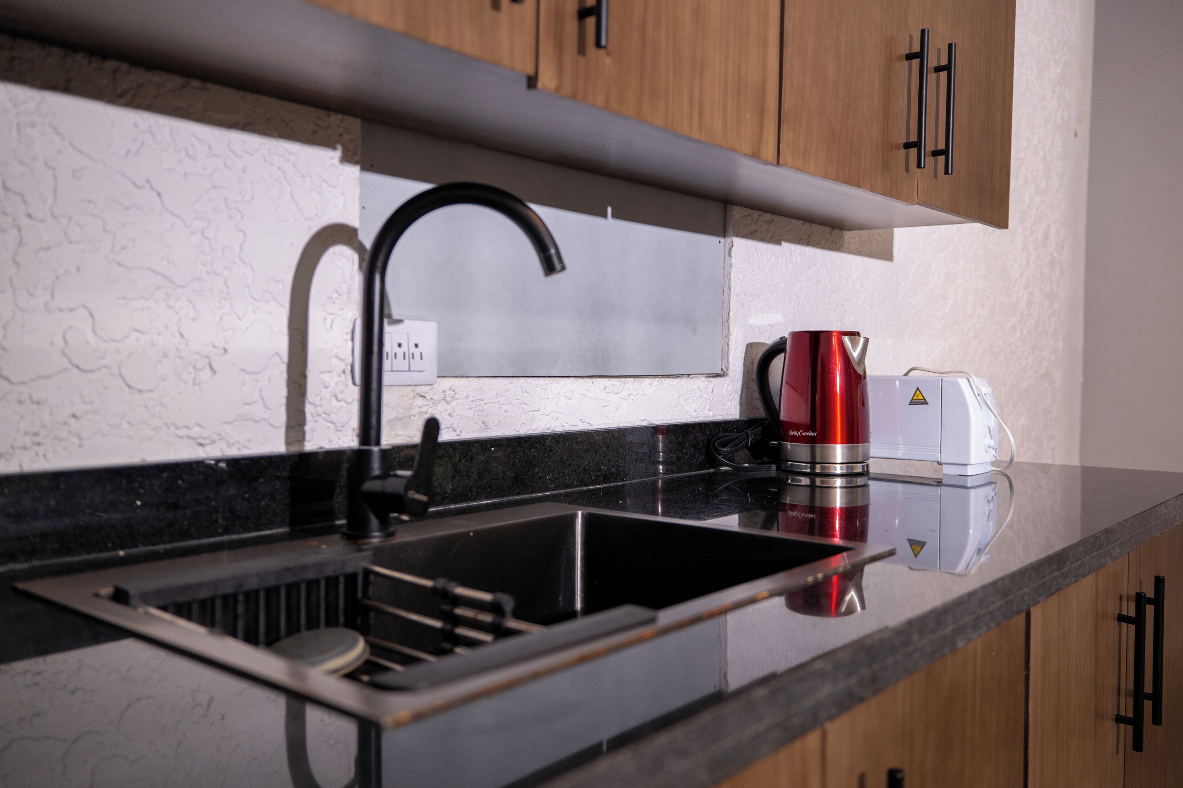Una cocina con un lavabo negro, grifo de acero inoxidable y hervidor rojo.