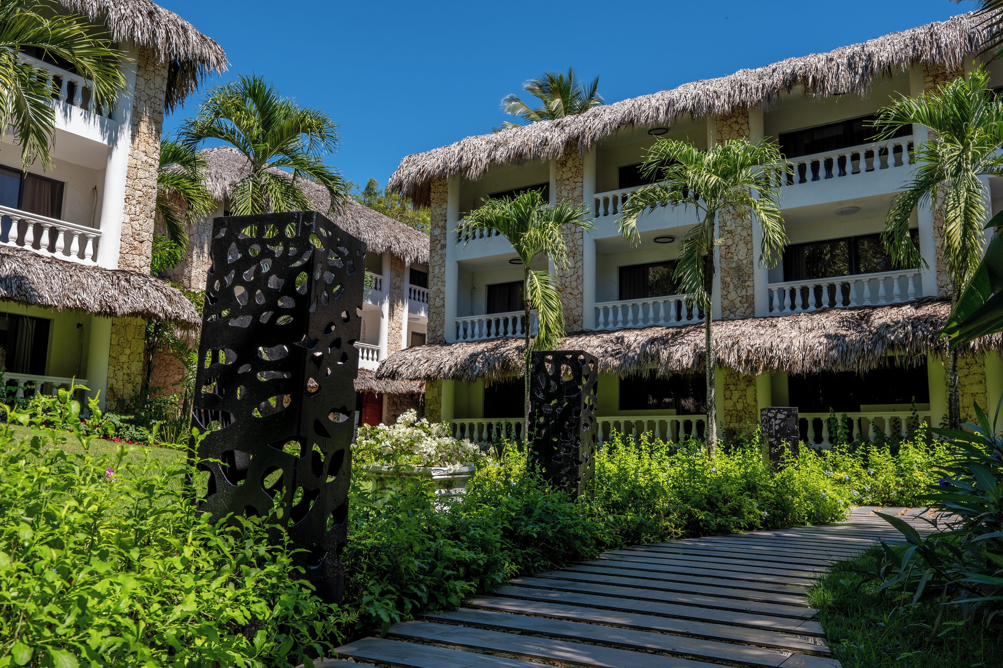 Ein Resort mit strohgedeckten Gebäuden, einem Holzweg und üppiger Vegetation.
