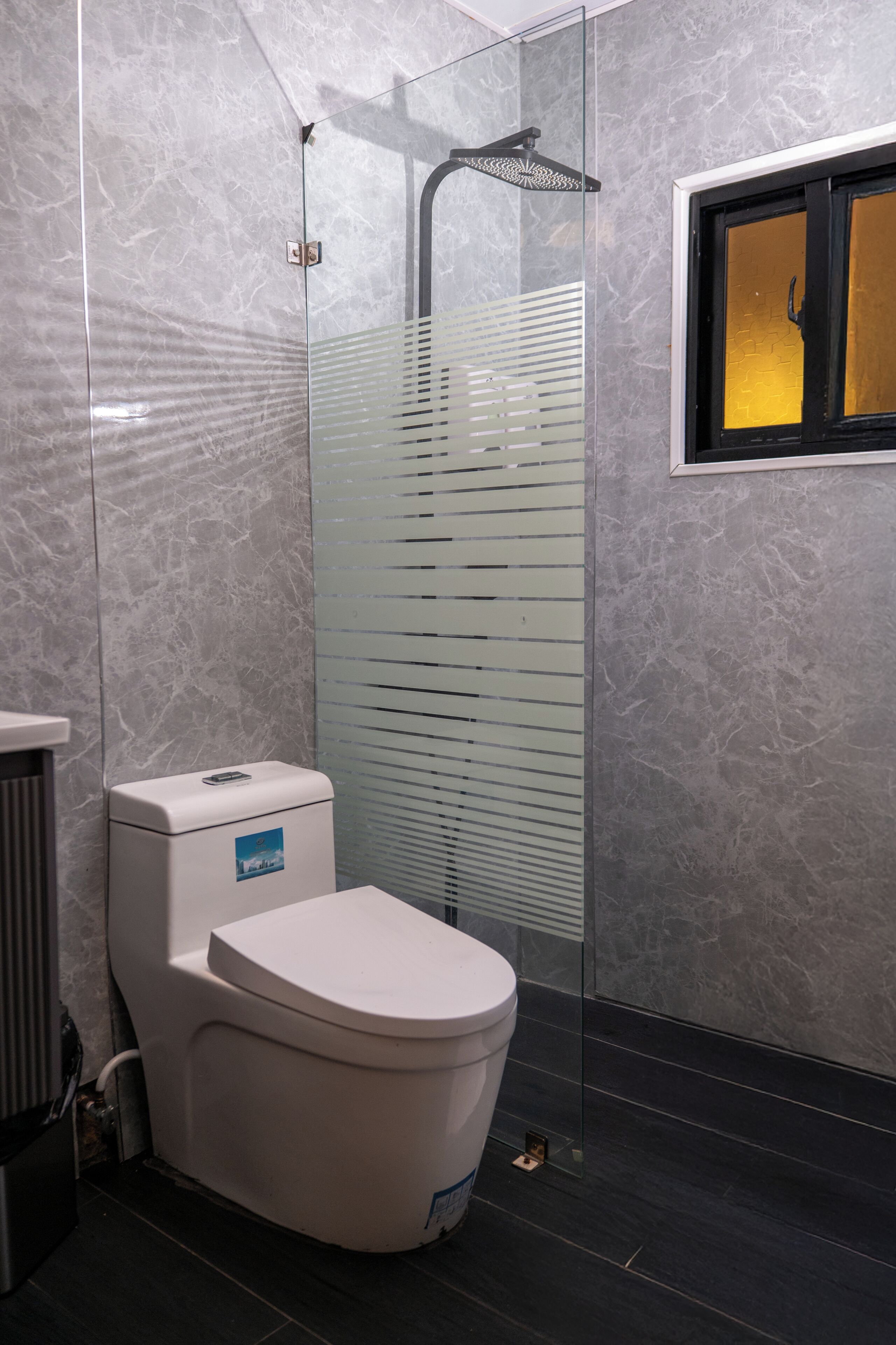 A modern bathroom with a glass-enclosed shower, a white toilet, and a marble wall.