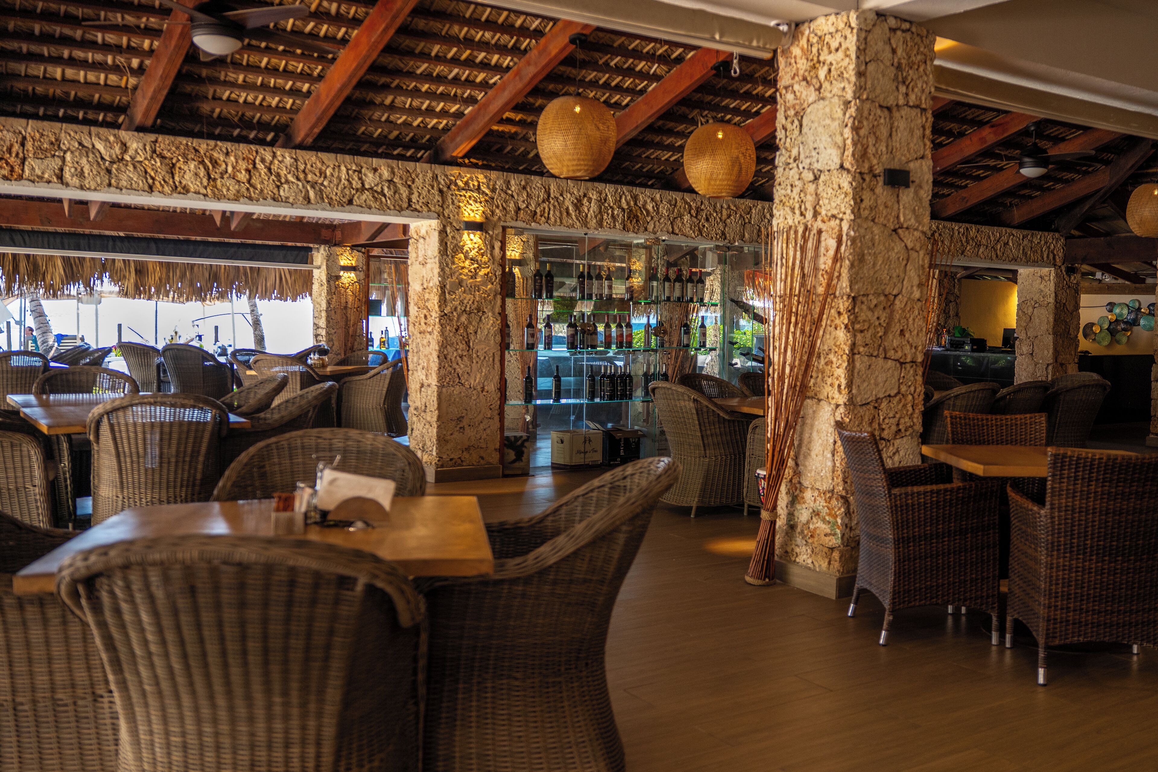 Un restaurante con mobiliario de mimbre, pilares de piedra y una zona de bar.